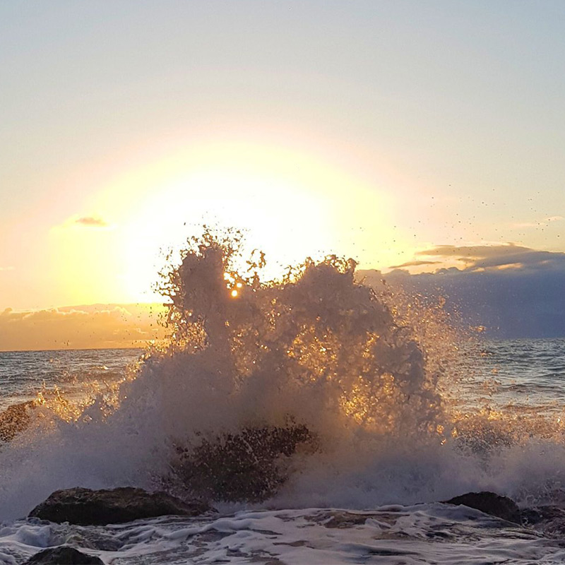 Eine Welle bricht vor der aufgehenden Sonne an einem Felsen