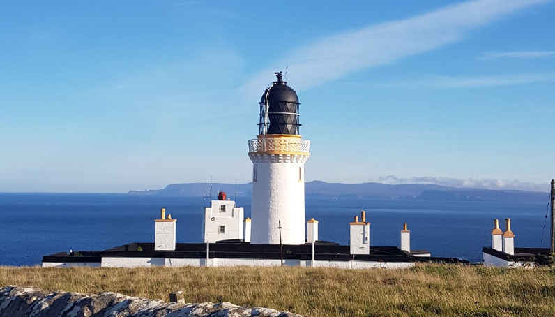 Ein weißer Leuchtturm weist Schiffen an einem sonnigen Tag den Weg.
