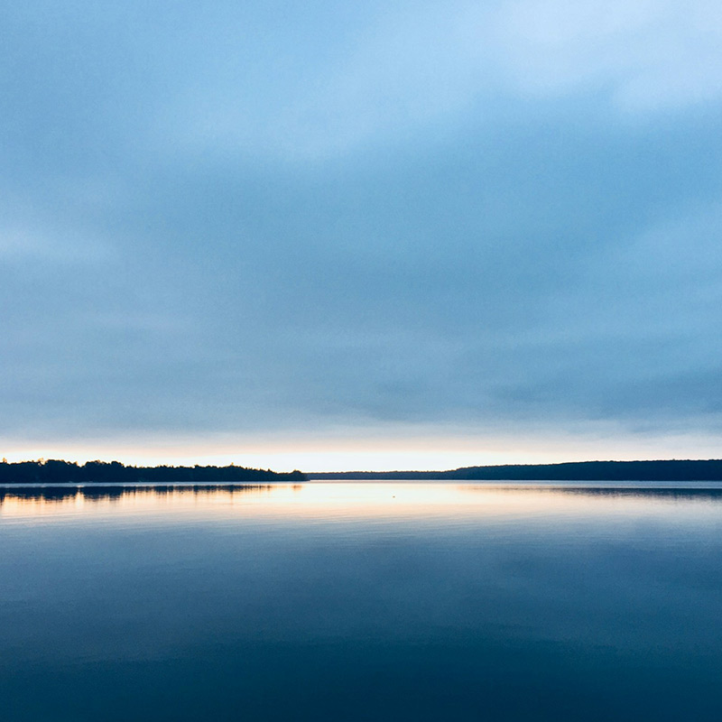 Ein See liegt mit spiegelglatter Oberfläche in der Dämmerung